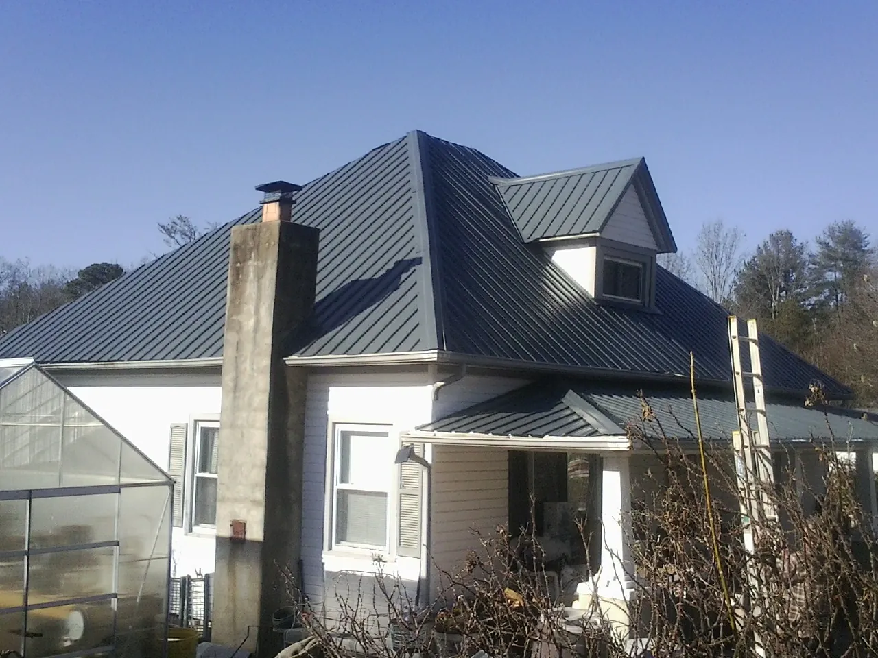 Dark blue standing seam metal roof on a white farmhouse with dormer — Slate & Tile Roof Repair by Roofing Brothers in Niceville
