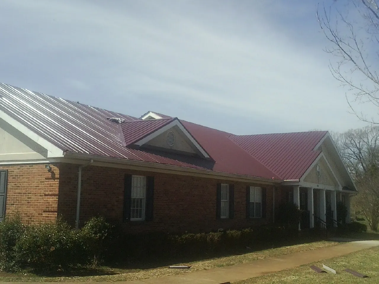 Red metal roof with gabled entries on a long brick building, from a Hail Damage Roof Repair job in Niceville