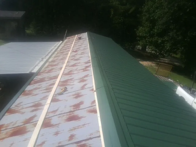 Old rusted panels beside newly installed green metal roofing — Wind Damage Roof Repair by Roofing Brothers in Niceville