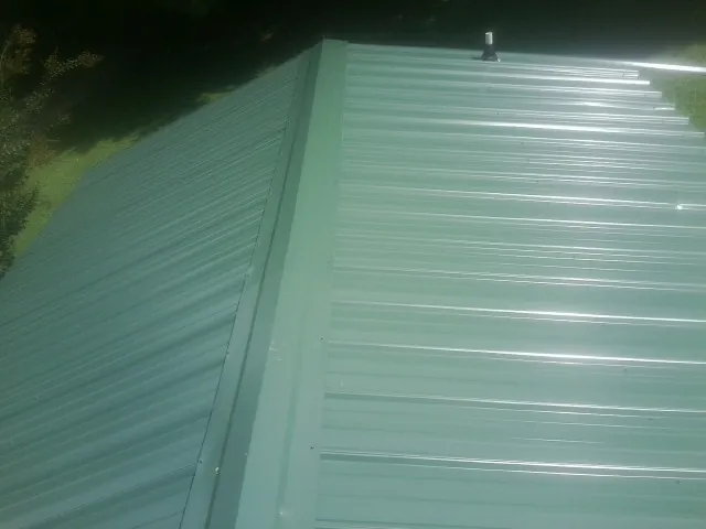 New green metal panels meeting at the ridge of a roof — Flat Roof Repair work by our crew in Niceville