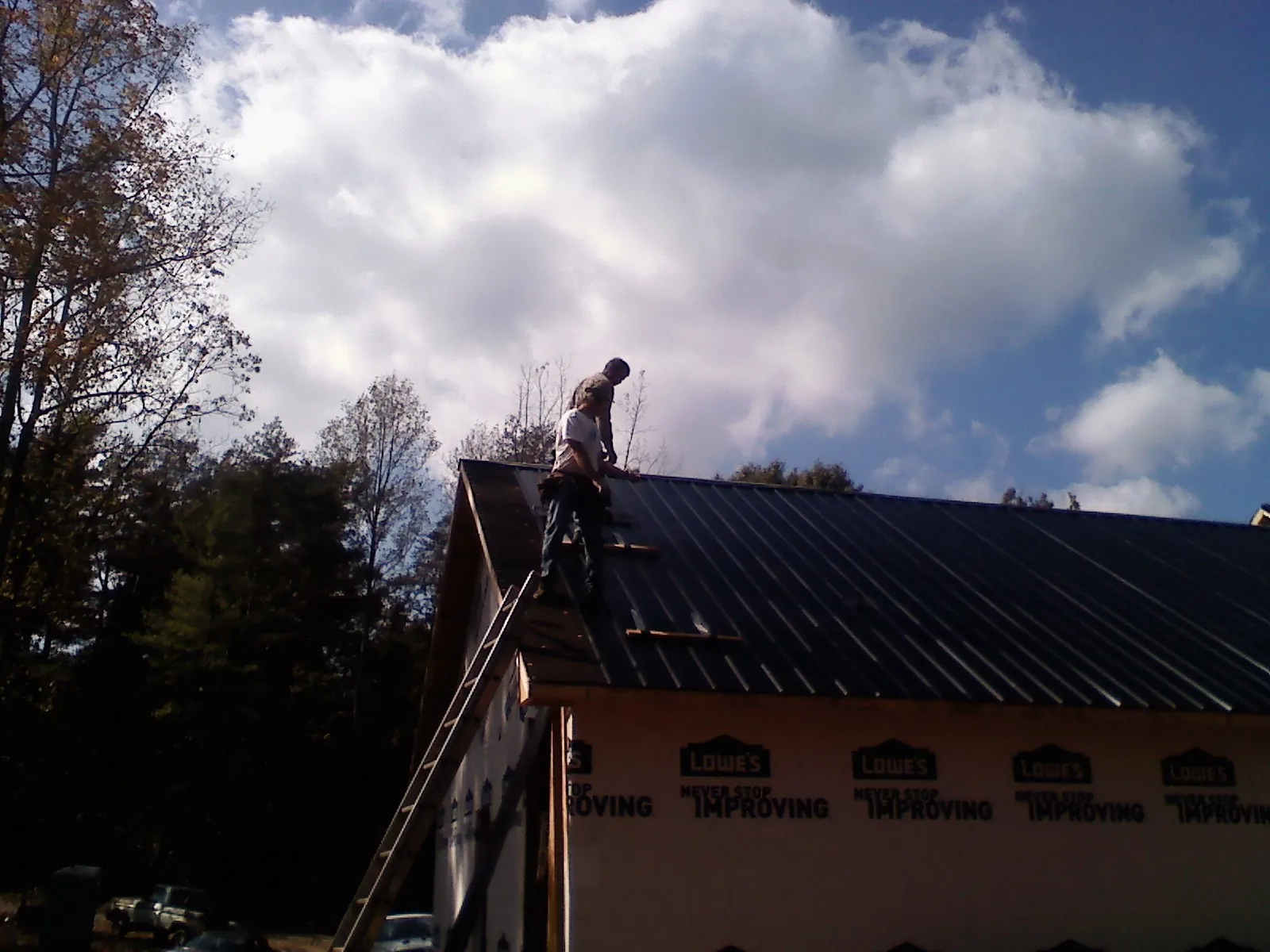 Roofer fastening dark metal panels high against a cloudy sky, from a Roof Inspection job in Niceville