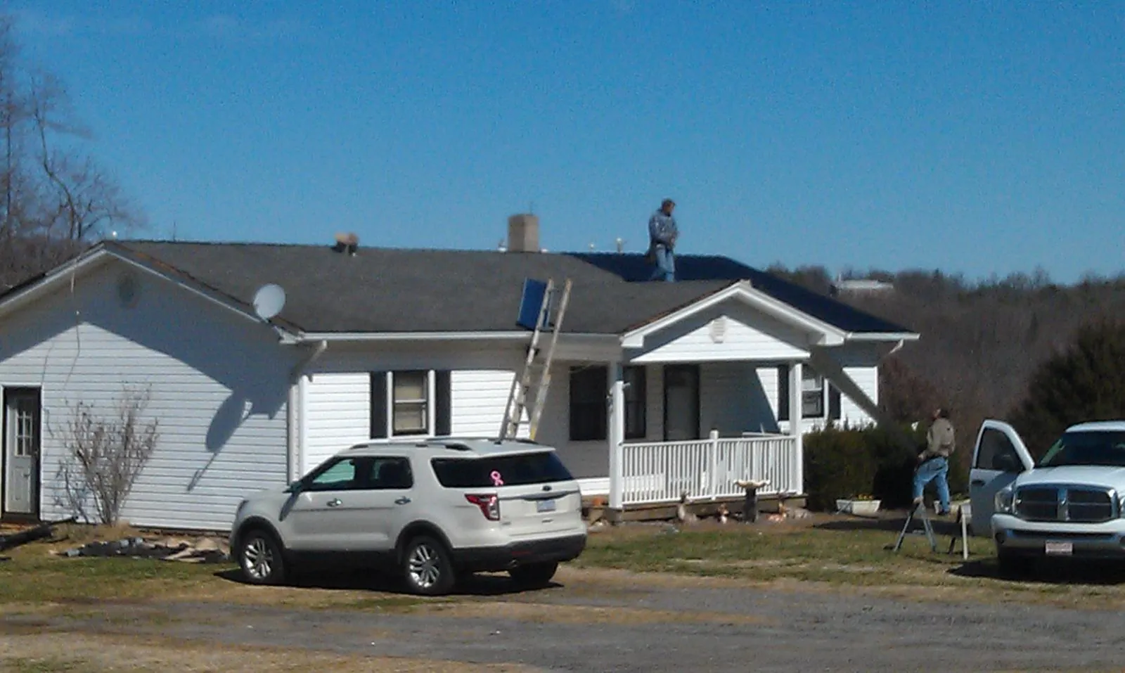 Roofers stripping shingles from a white ranch house roof in Niceville