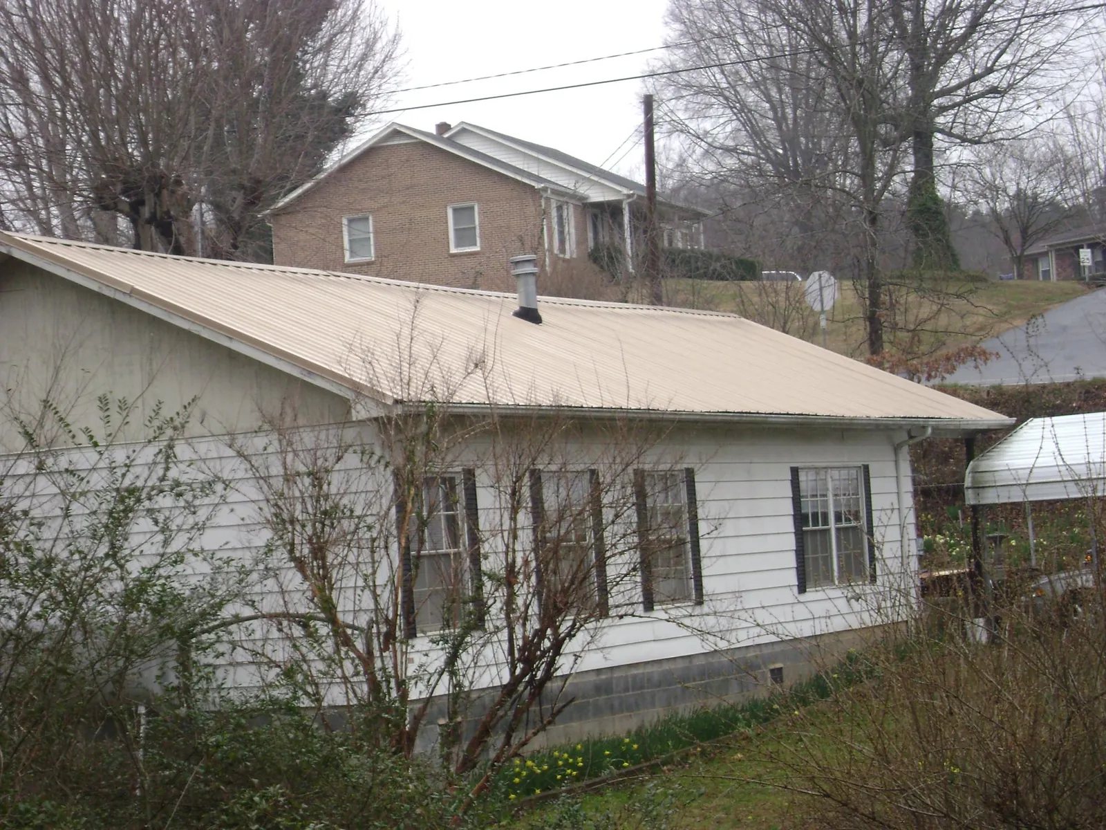 Tan metal roof on a white sided house set into a hillside — Commercial Roofing by Roofing Brothers in Niceville